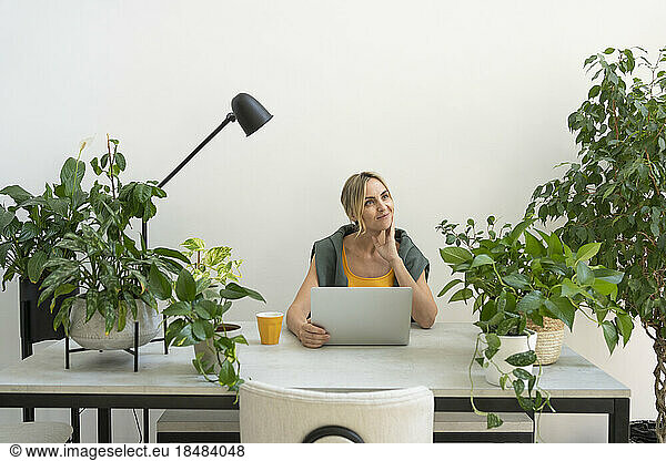 Thoughtful freelancer sitting with laptop at desk