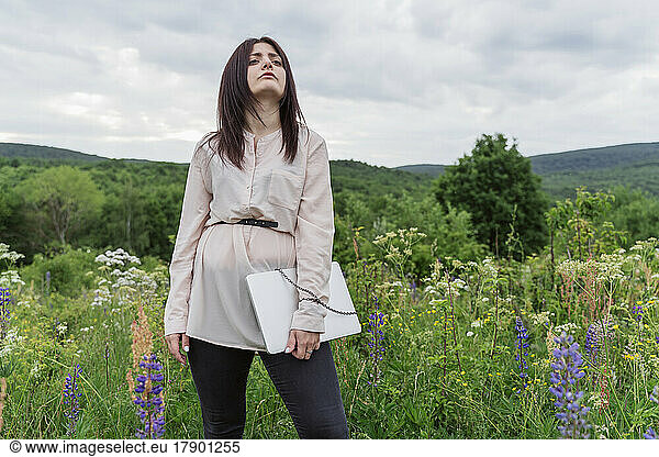 Thoughtful freelancer trapped with laptop amidst lupine flowers