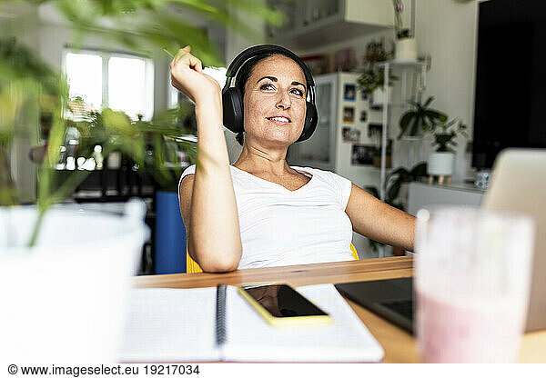 Thoughtful freelancer wearing wireless headphones sitting at desk