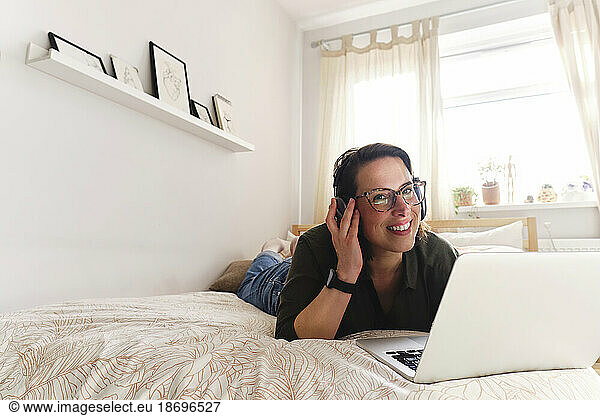 Thoughtful freelancer with laptop lying on bed at home