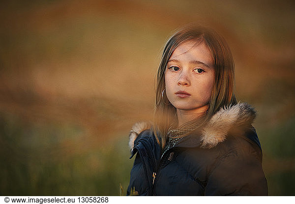Thoughtful girl in warm clothing on field during sunset