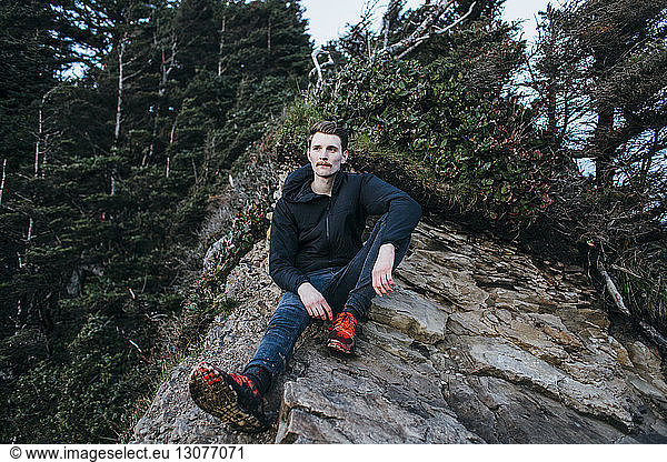 Thoughtful hiker sitting on rock against trees