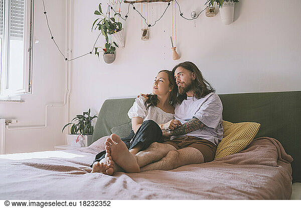Thoughtful hipster couple sitting on bed at home