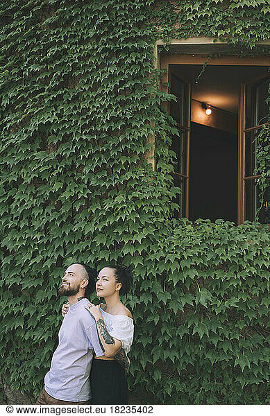 Thoughtful hipster couple standing in front of green ivy plants