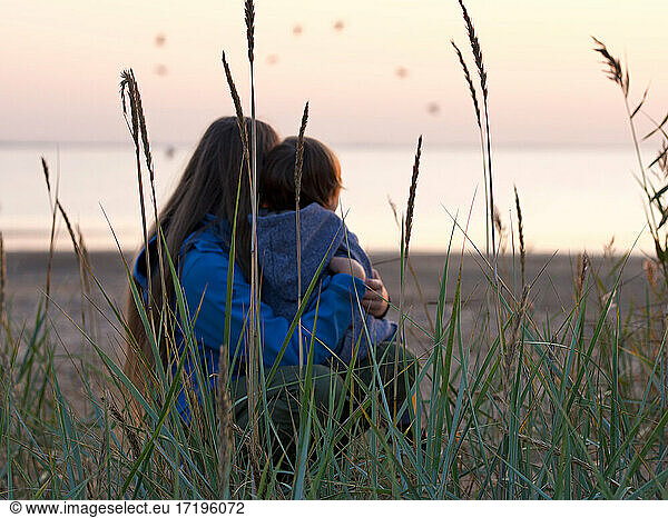 Thoughtful hugging siblings while sitting at beach  focus on cane