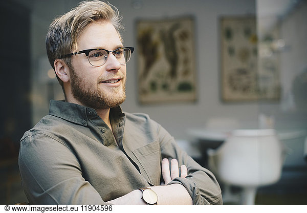 Thoughtful male computer programmer standing arms crossed in office