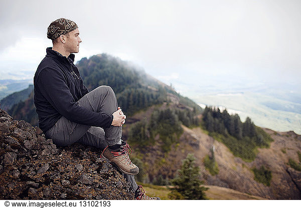 Thoughtful male hiker sitting on mountain