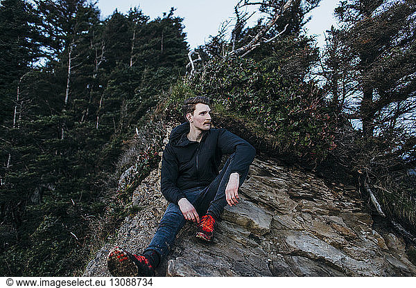 Thoughtful male hiker sitting on rock against trees