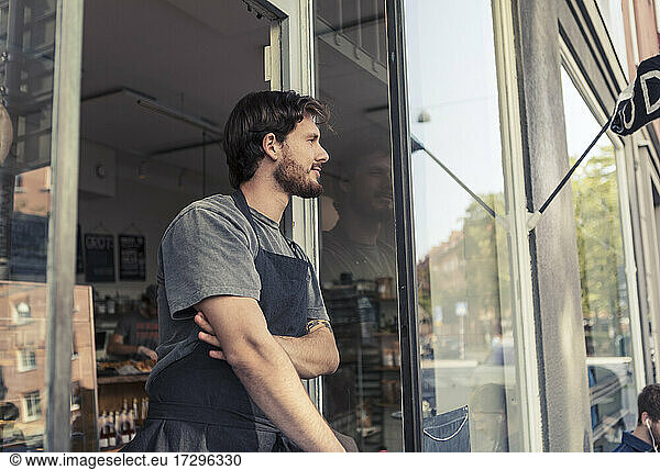 Thoughtful male owner looking away while standing at cafe entrance