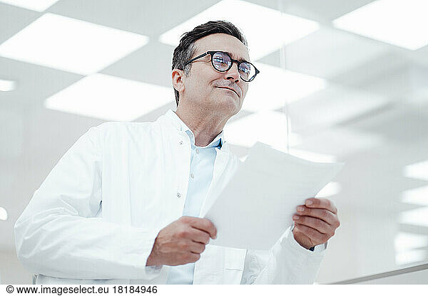 Thoughtful man in lab coat holding document in laboratory