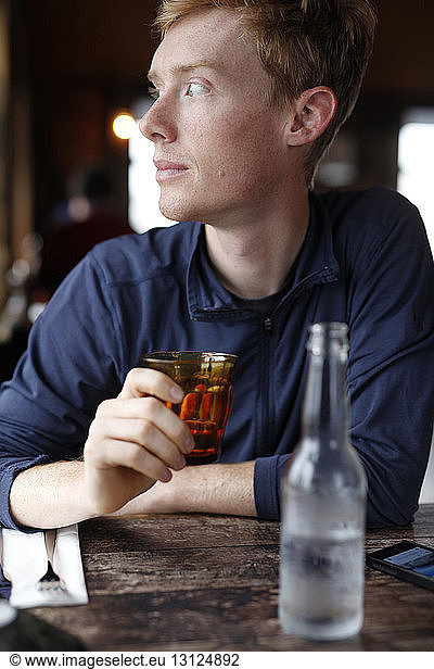 Thoughtful man looking away while holding drinking glass at restaurant