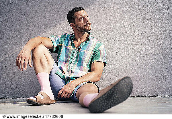 Thoughtful man sitting on floor near concrete wall