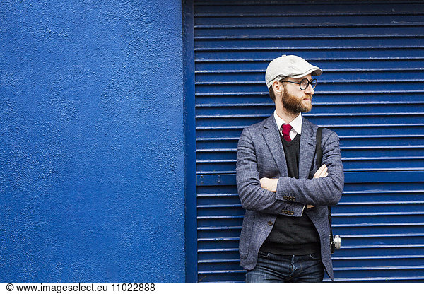 Thoughtful man standing arms crossed against blue shutter