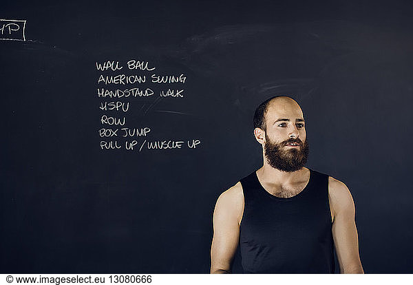 Thoughtful man trainer standing against blackboard in gym
