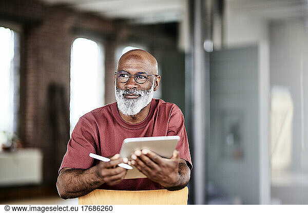 Thoughtful man with digitized pen and tablet computer at home