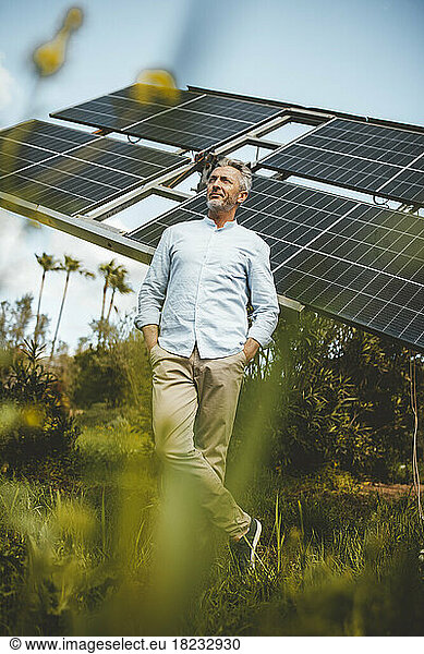 Thoughtful man with hands in pockets standing by solar panels