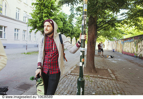 Thoughtful man with skateboard standing on sidewalk