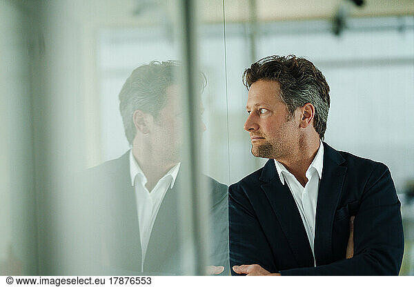 Thoughtful mature businessman looking through glass wall