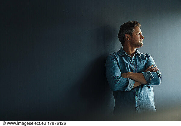 Thoughtful mature businessman standing in front of wall