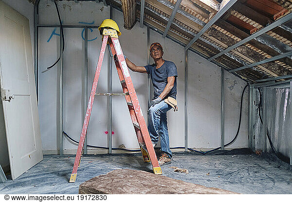 Thoughtful mature construction worker standing by ladder at site