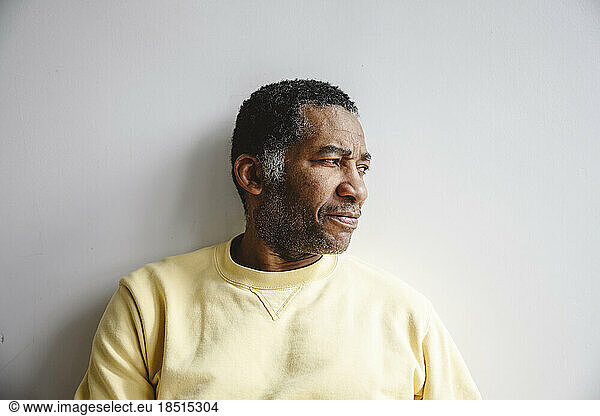 Thoughtful mature man leaning on white wall