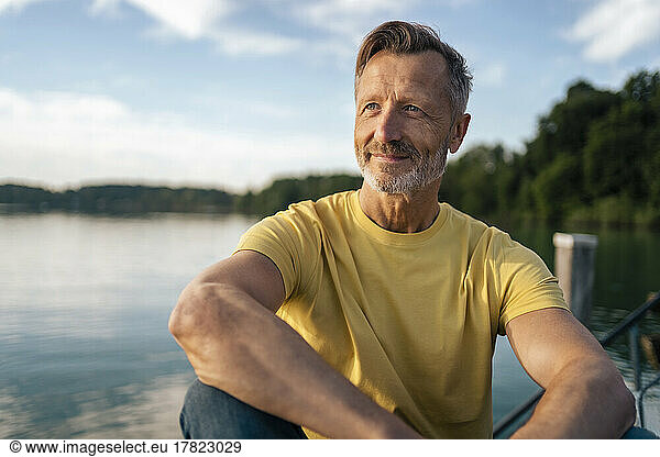 Thoughtful mature man sitting at lake on sunny day