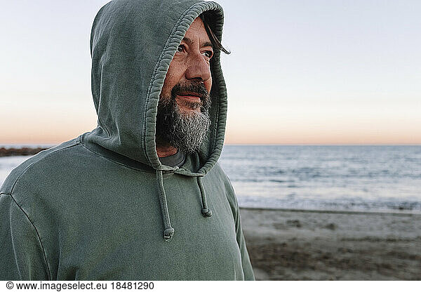 Thoughtful mature man wearing hood at beach