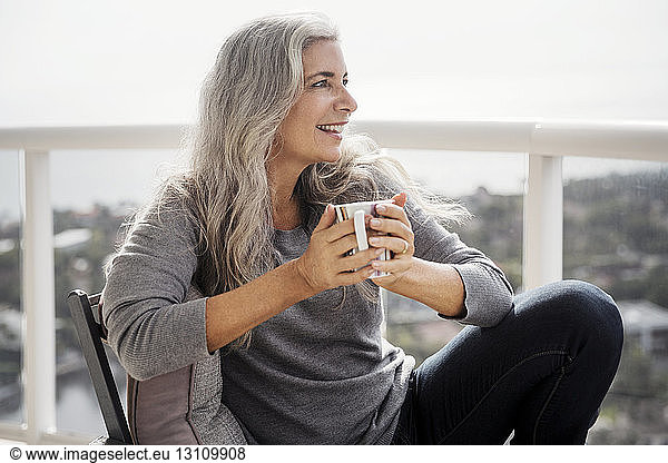 Thoughtful mature woman holding coffee mug while sitting on balcony