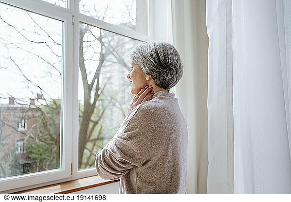 Thoughtful mature woman looking through window at home