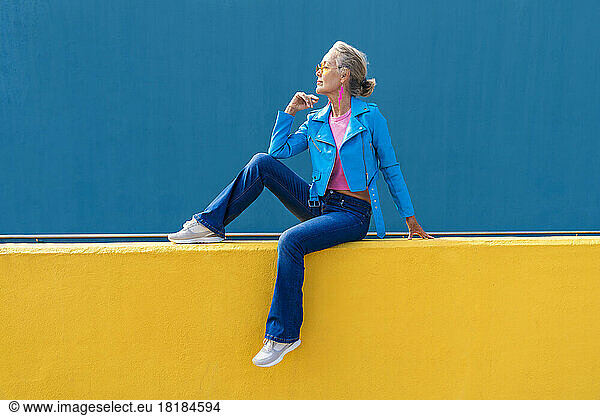 Thoughtful mature woman on yellow wall
