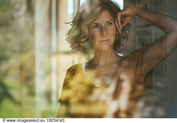 Thoughtful mature woman seen through glass window
