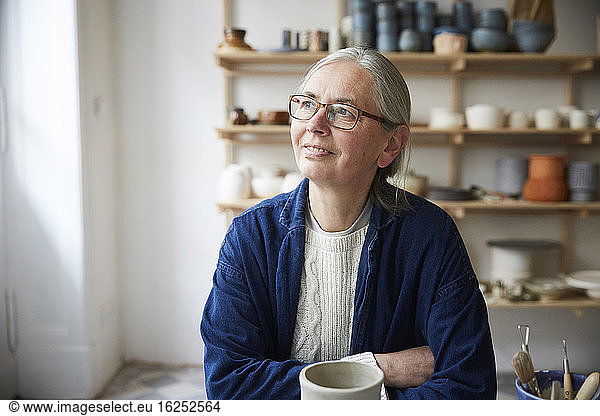 Thoughtful mature woman sitting in pottery class