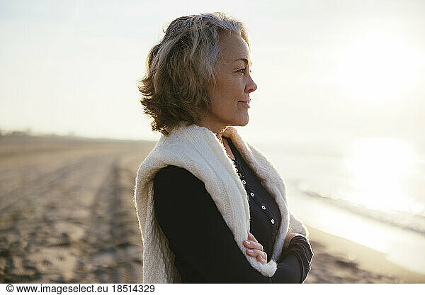 Thoughtful mature woman with arms crossed standing at beach