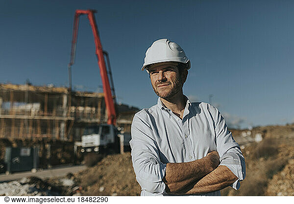 Thoughtful mature worker with arms crossed standing at construction site