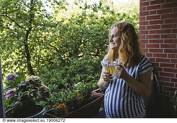 Thoughtful pregnant woman holding herbal tea cup in balcony