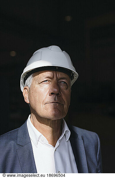 Thoughtful senior businessman wearing hard hat in factory