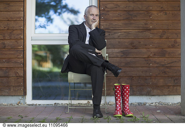 Thoughtful senior businessman wearing suit and sitting at street  Freiburg im Breisgau  Baden-Württemberg  Germany
