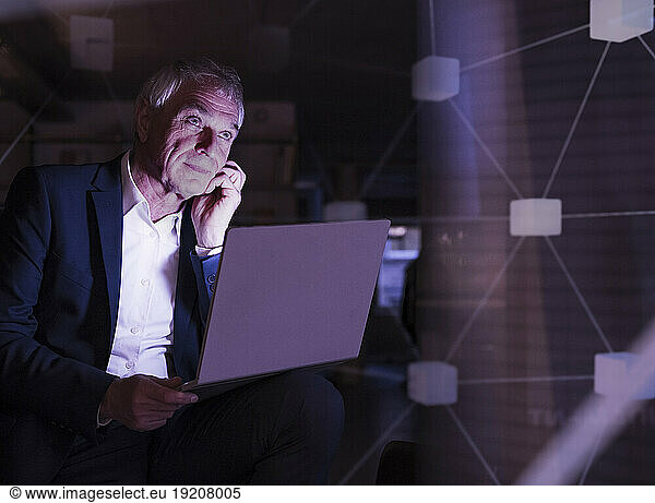 Thoughtful senior businessman with laptop in office