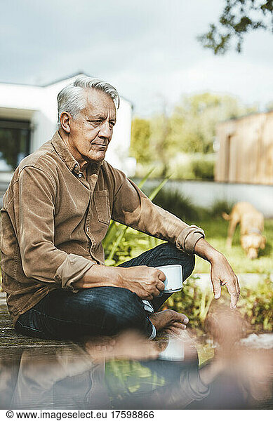 Thoughtful senior man holding coffee cup sitting at backyard