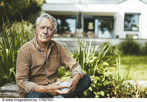 Thoughtful senior man holding coffee cup sitting in garden