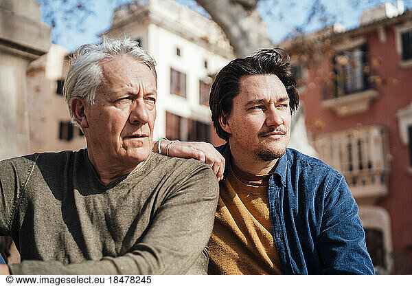 Thoughtful senior man sitting with son in front of building
