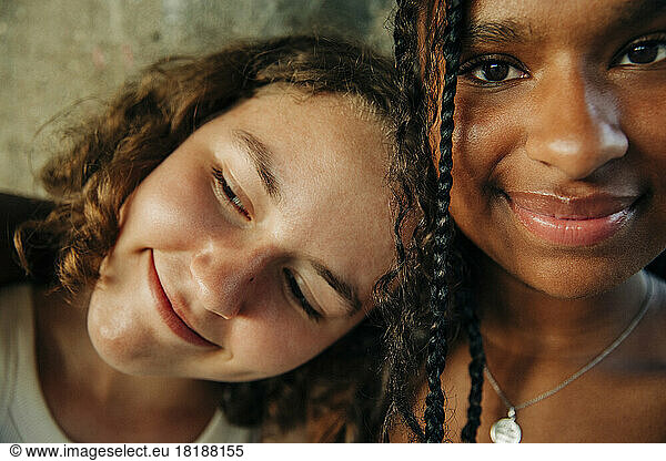 Thoughtful smiling teenage girl leaning head on female friend