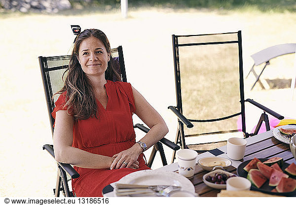 Thoughtful smiling woman sitting at table on folding chair at campsite