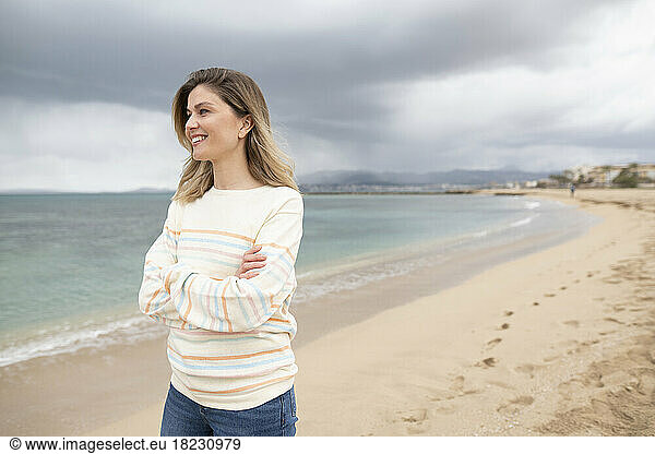 Thoughtful smiling woman with arms crossed walking at beach