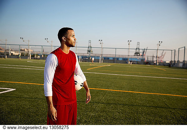 Thoughtful sportsman with soccer ball standing on field