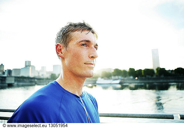Thoughtful sporty man standing by river in city