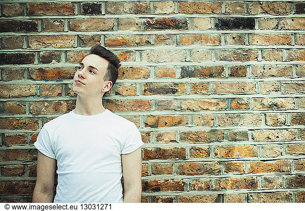 Thoughtful teenage boy standing at brick wall
