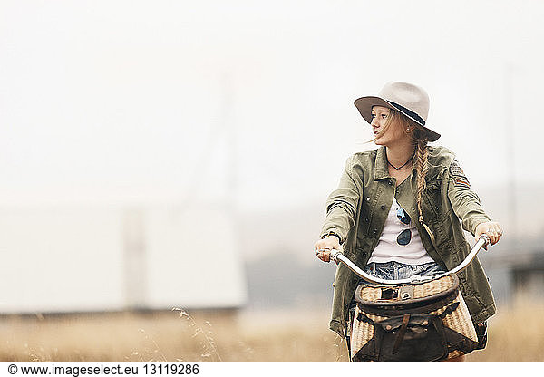 Thoughtful teenage girl looking away while riding bicycle on field