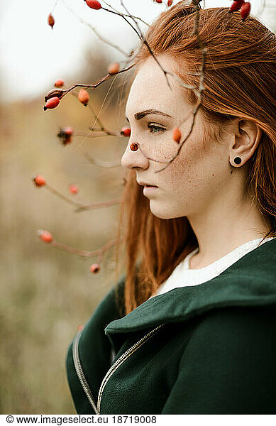 Thoughtful teenage girl with red head standing amidst plants