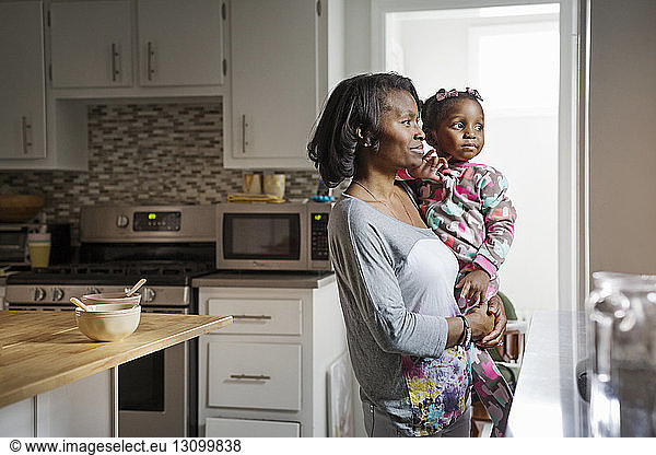 Thoughtful woman carrying daughter in kitchen